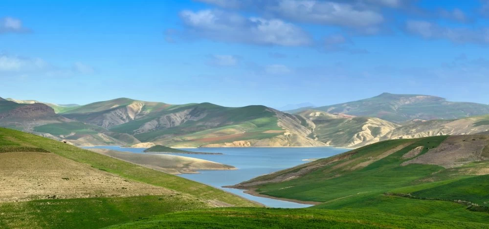 Panorama of moroccan landscape with green fielda, bid lake and Atlas mountains on background