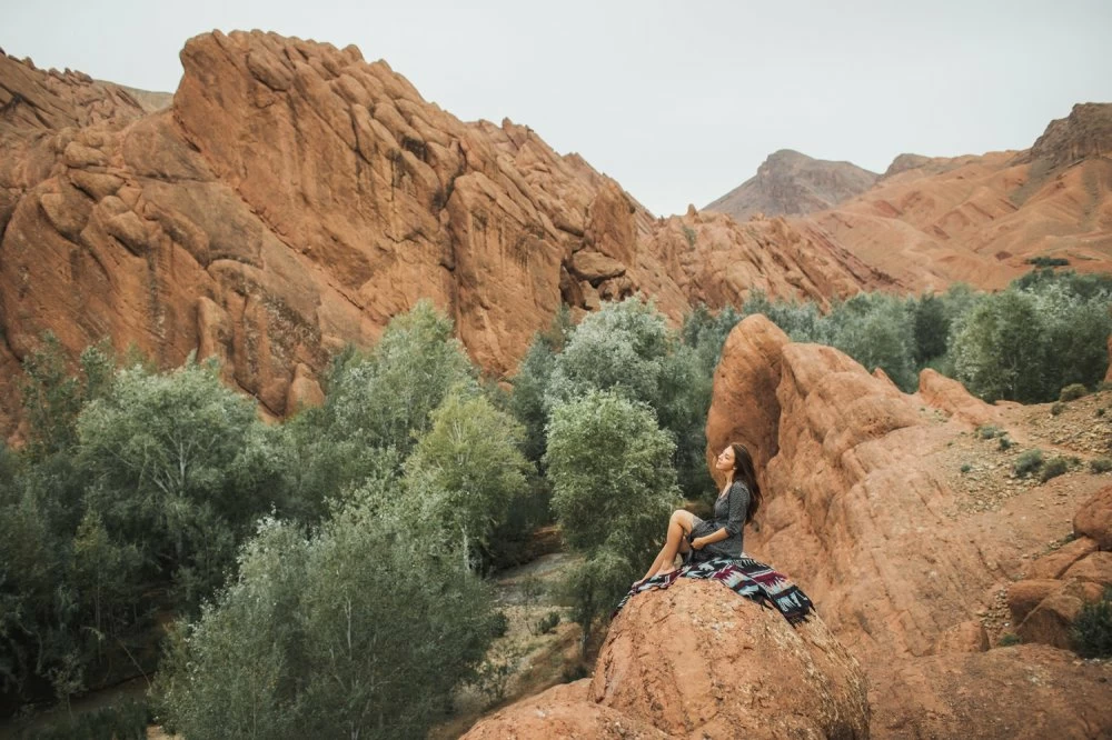 Woman sitting on oriental carpet on background of Todra gorge canyon in Morocco. Harmony with nature and freedom concept. Hippie lifestyle.