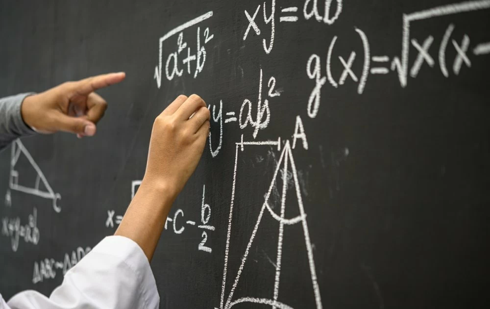 The hand that is written with the white chalk and the hand that shows the formula on the blackboard.